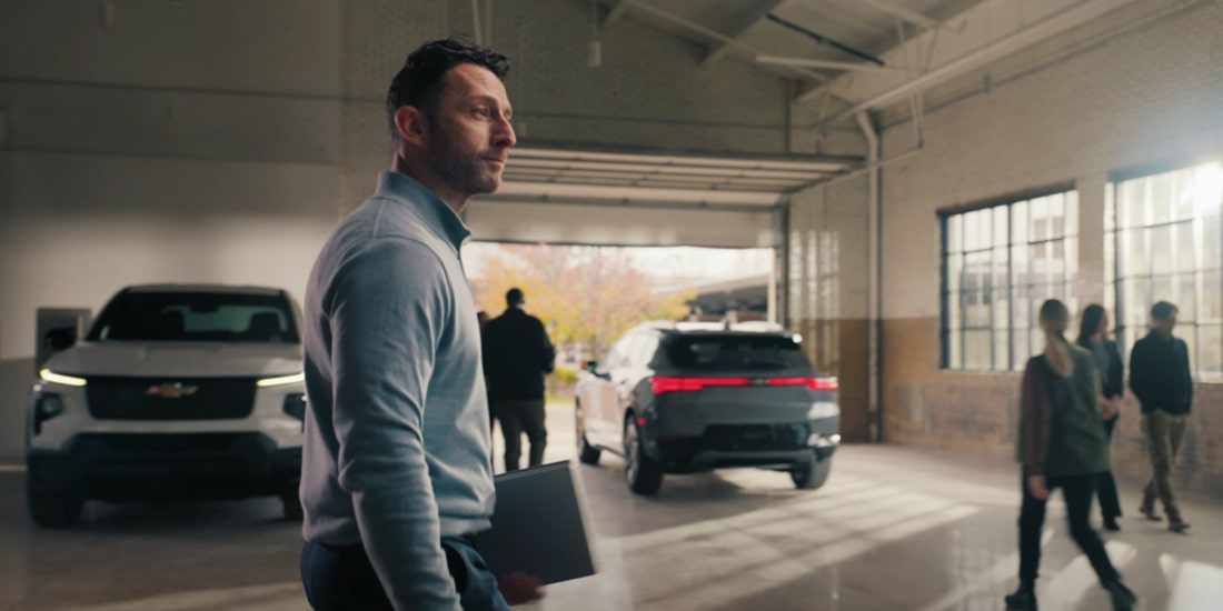 A thumbnail for the OnStar EV Reimbursement Video displaying a man walking past two GM vehicles