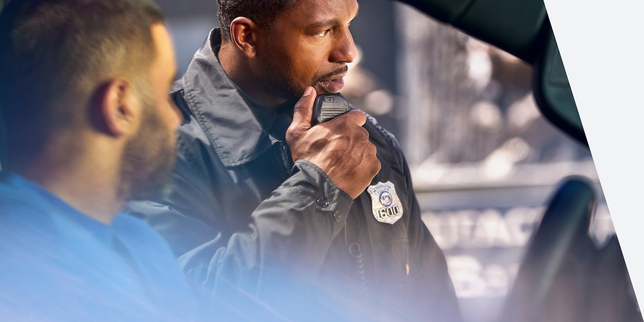 Police officer speaking on radio with person in car in front of them