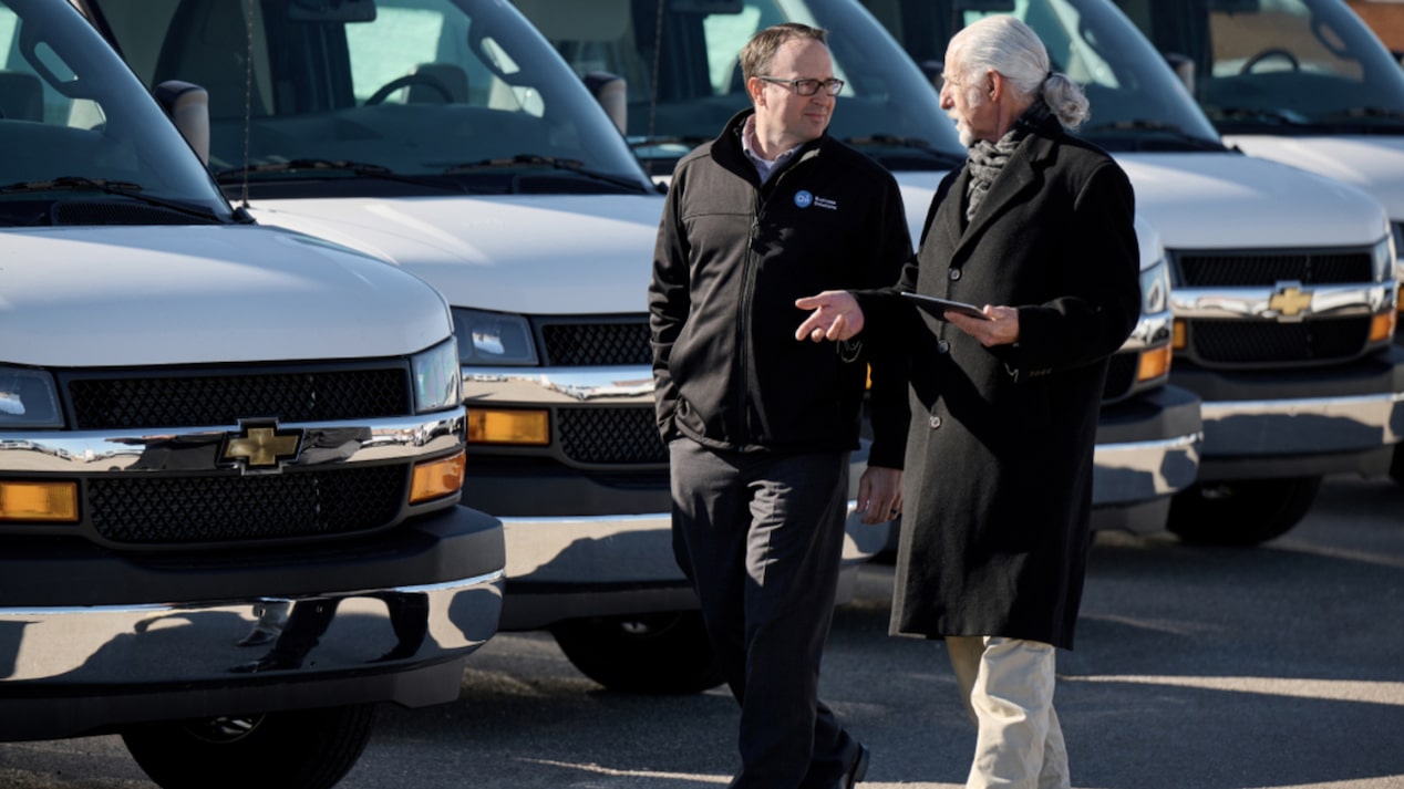 Two People Walking Side by Side Having a Conversation with Vehicles in the Background