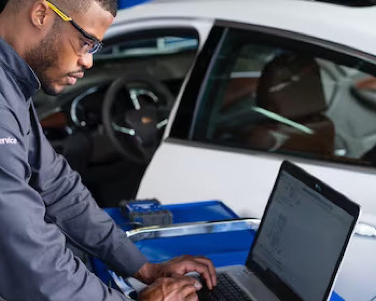 Certified Service Technician Working on a Laptop Next to a Vehicle