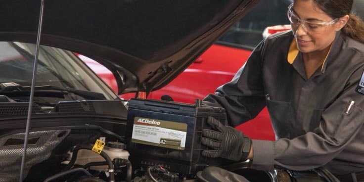 A worker installing a battery in the front of a car