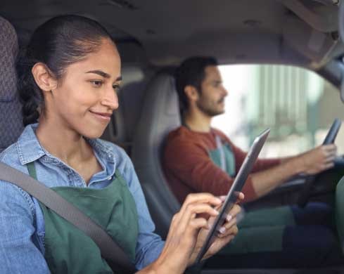 Two People Sitting in a Car with the Passenger Looking at a Tablet